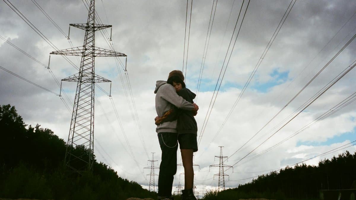 Couple hugging beneath power lines under a cloudy sky, showcasing a moment of affection and connection.