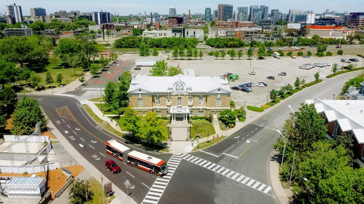 Aerial shot of a city intersection with a historic building and urban skyline in the background.