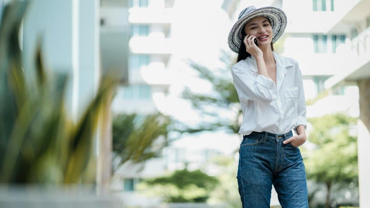 Smiling woman in straw hat making a phone call outdoors, enjoying a sunny day.