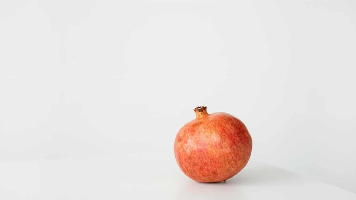 A single pomegranate on a white surface, minimalist still life shot.