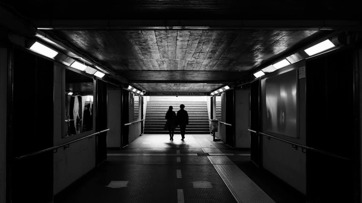 Back view black and white of unrecognizable passengers walking to stairs in subway station