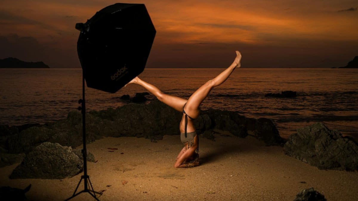 A person performs a yoga headstand on a sandy beach in Ranong, Thailand, during a beautiful sunset.