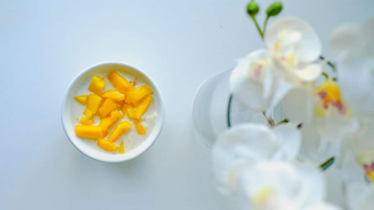 A flat lay of a bowl of mango yogurt with white orchid flowers, perfect for a healthy breakfast.