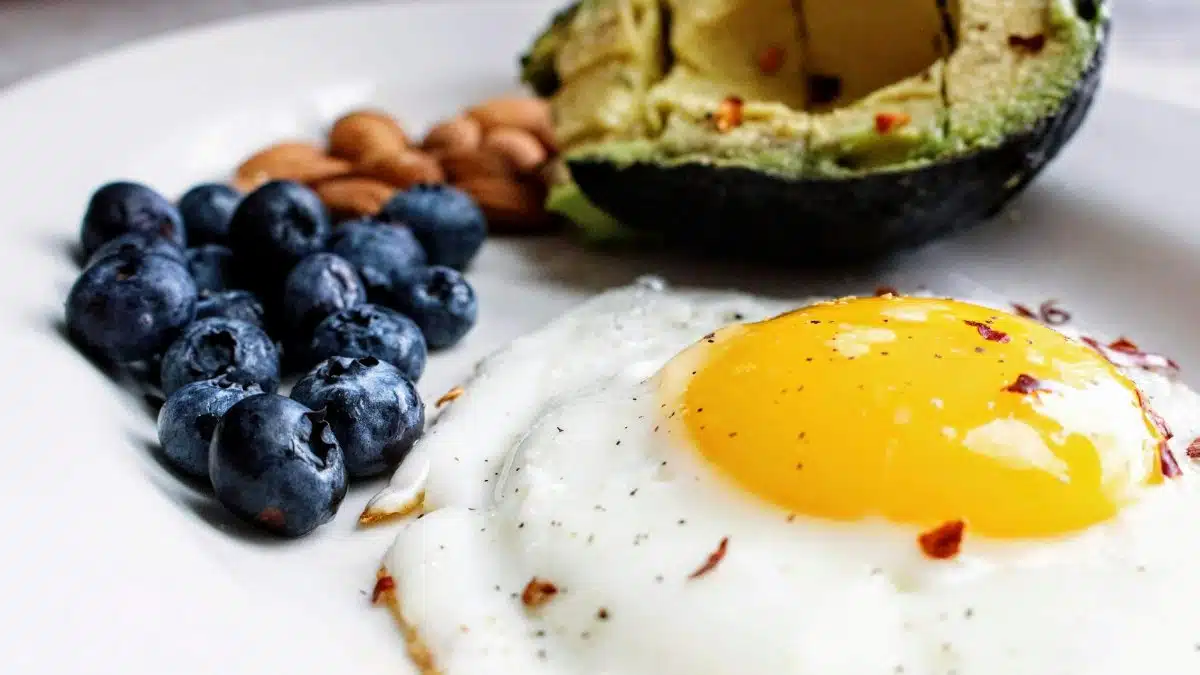 A nutritious breakfast featuring a fried egg, avocado, blueberries, and almonds.