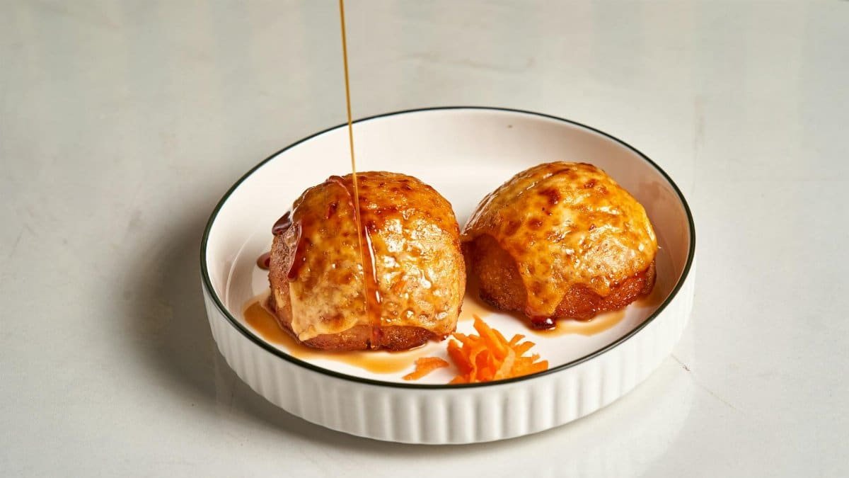 Baked pastries drizzled with honey, served on a white plate with carrot garnish.