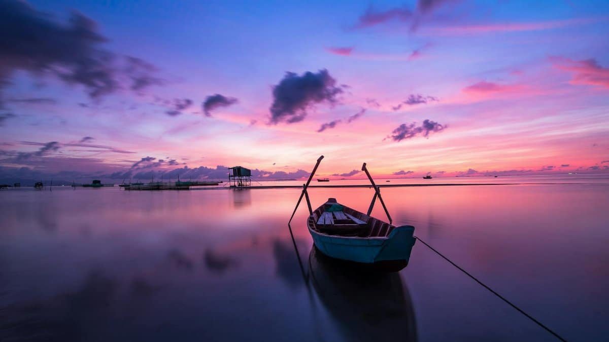 A tranquil tropical sunrise with a lone boat on calm waters.