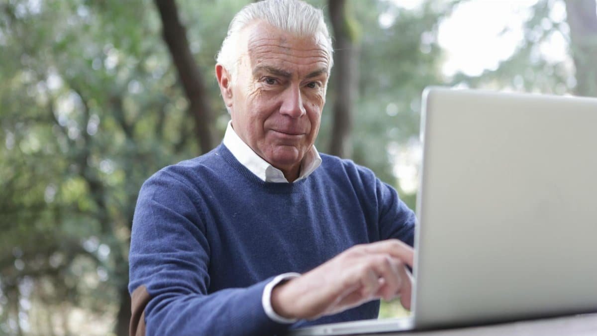 Senior man enjoying remote work on a laptop outdoors, embracing technology in nature.
