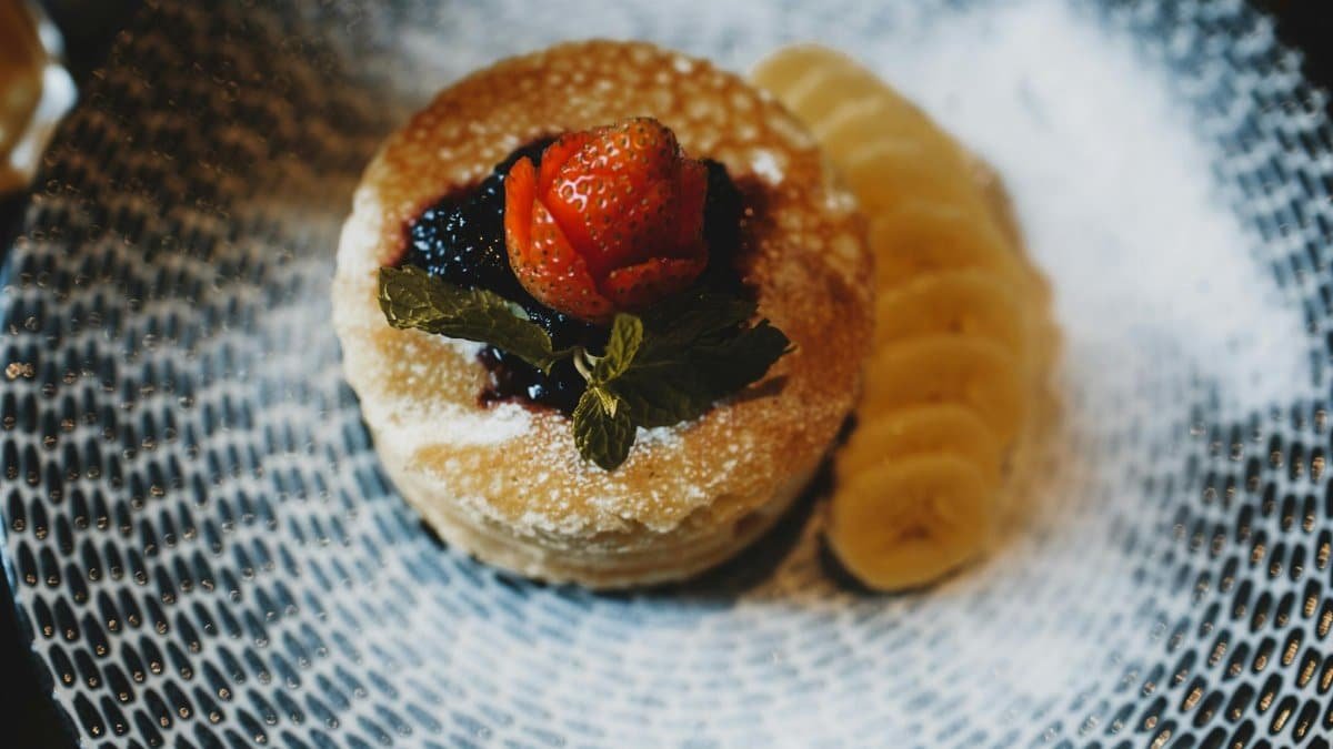 Appetizing pancake stack topped with strawberries, jam, and banana slices on a patterned plate.
