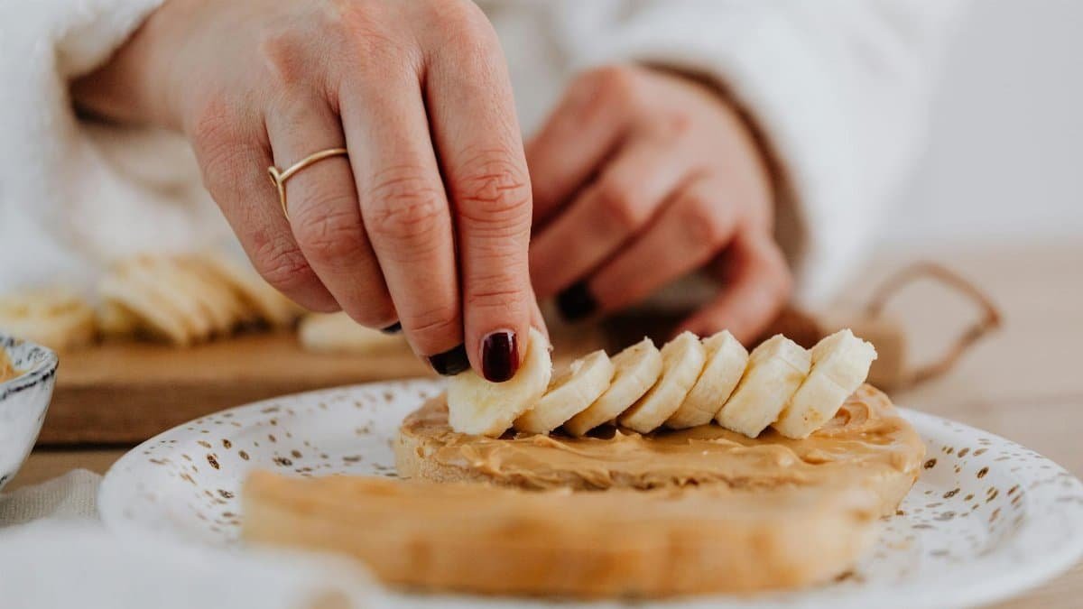 A hand places banana slices on peanut butter toast, highlighting a healthy snack preparation.