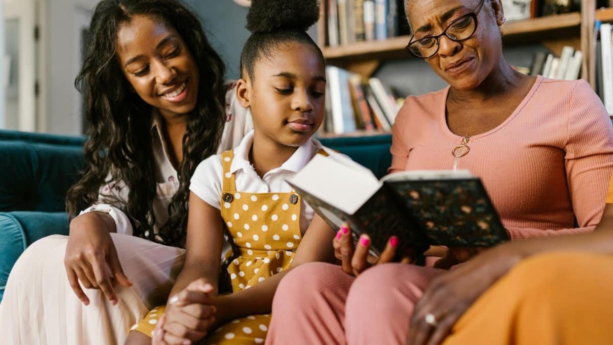 A joyful family gathering with three generations reading a book together indoors.