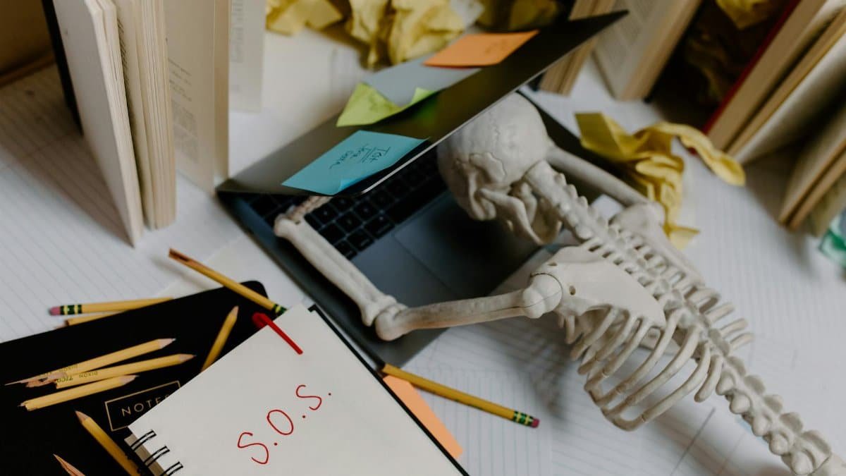 Dramatic still life of a skeleton overwhelmed at an untidy office desk with S.O.S. note.