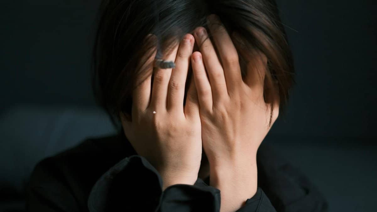 A woman with hands covering face showing emotion and stress indoors, creating a moody and introspective feel.
