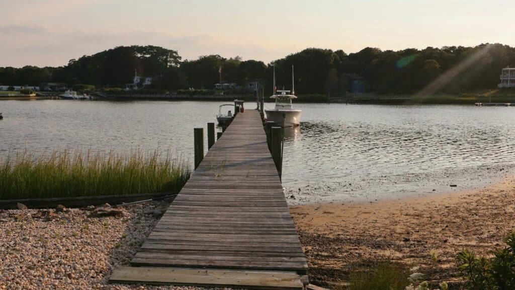 Serene wooden pier at sunset in Hampton Bays, NY, leading to calm waters.