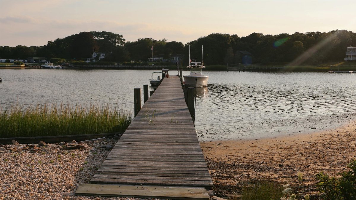 Serene wooden pier at sunset in Hampton Bays, NY, leading to calm waters.