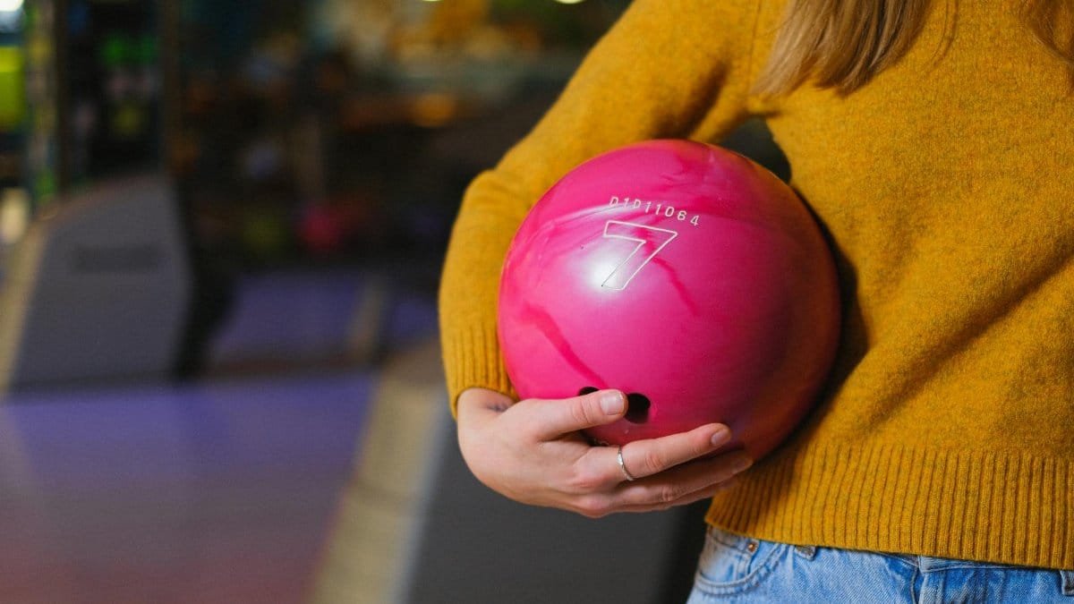 Close-up of a woman holding a pink bowling ball in a bowling alley. Weekend leisure activity indoors.