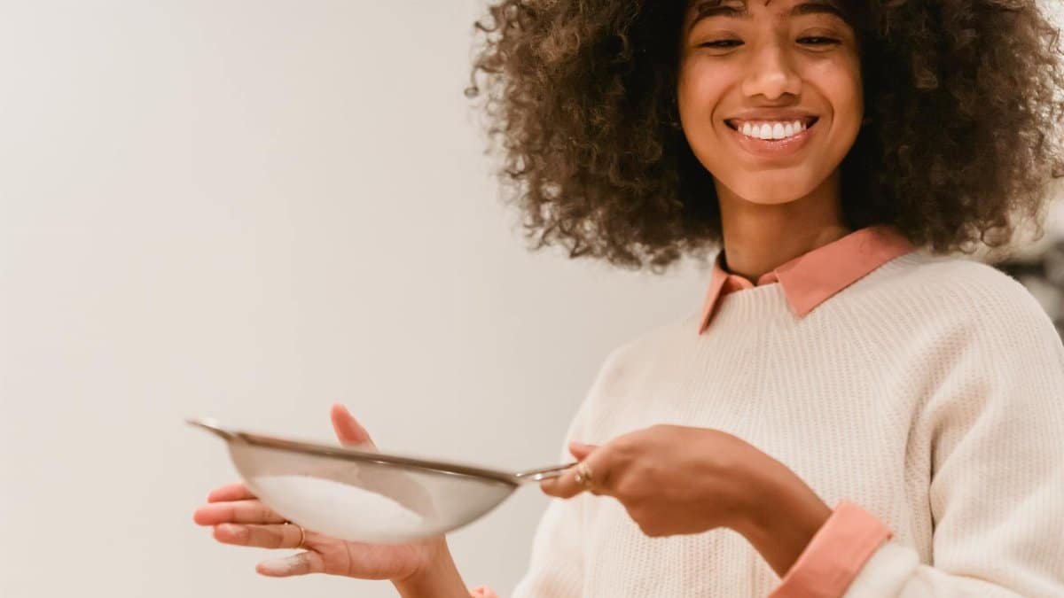 Happy woman with an afro sifting flour in a cozy kitchen setting, enjoying baking.