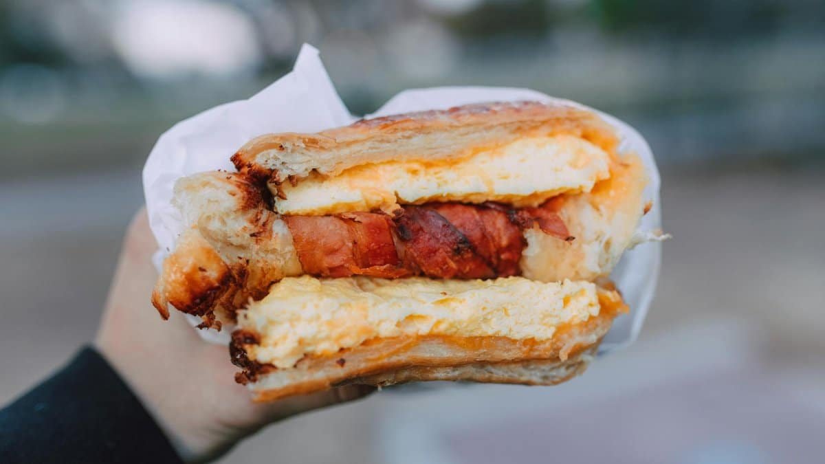 Close-up of a delicious breakfast sandwich with cheese and bacon held outside.