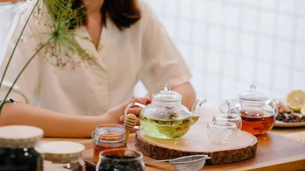 Woman enjoying a cozy tea time with herbal infusions and honey in a warm, inviting setting.