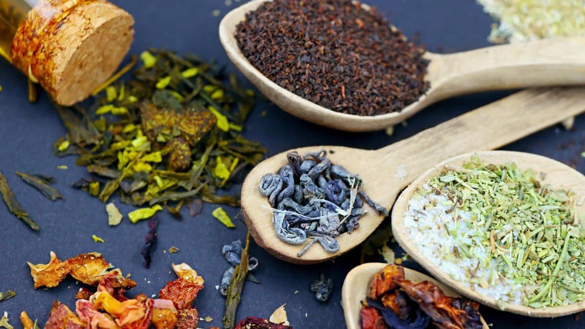 Assorted loose leaf herbal teas in wooden spoons on a flat lay composition, showcasing various colors and textures.