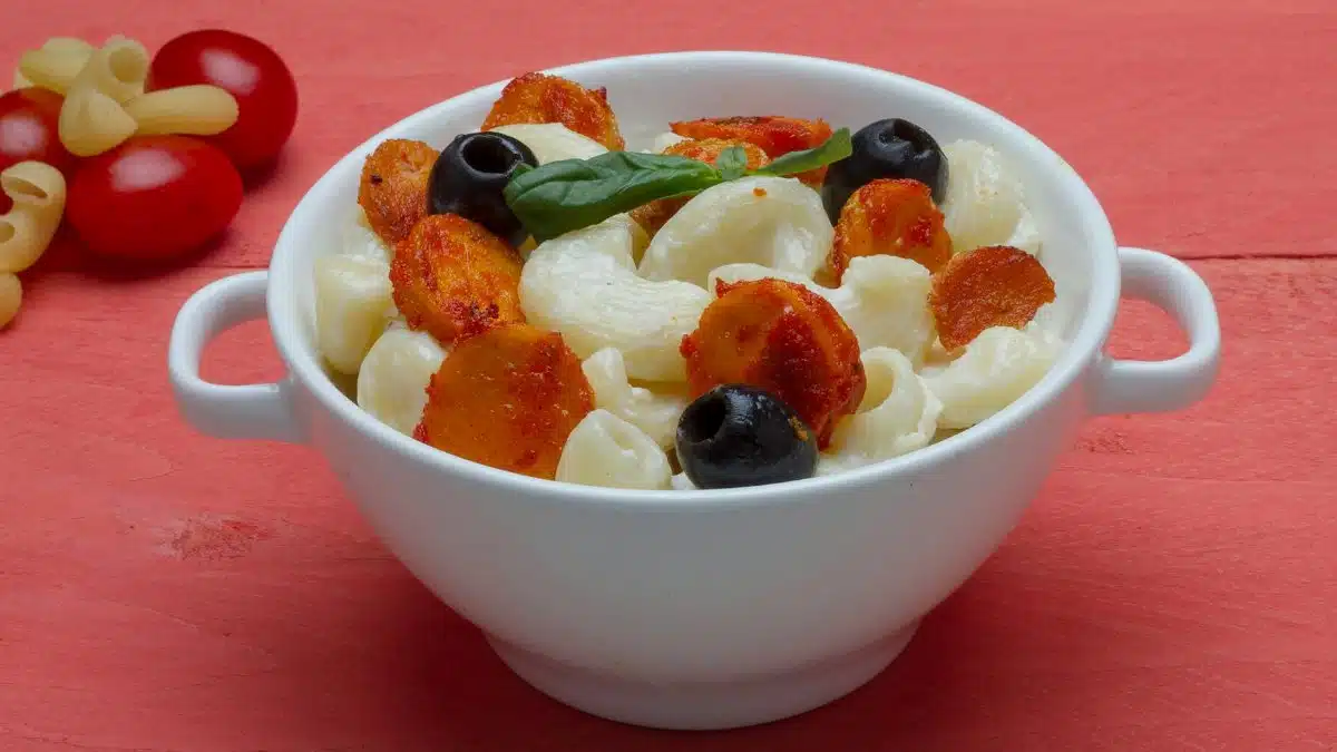Creamy pasta with olives and a hint of basil garnished on a red background.