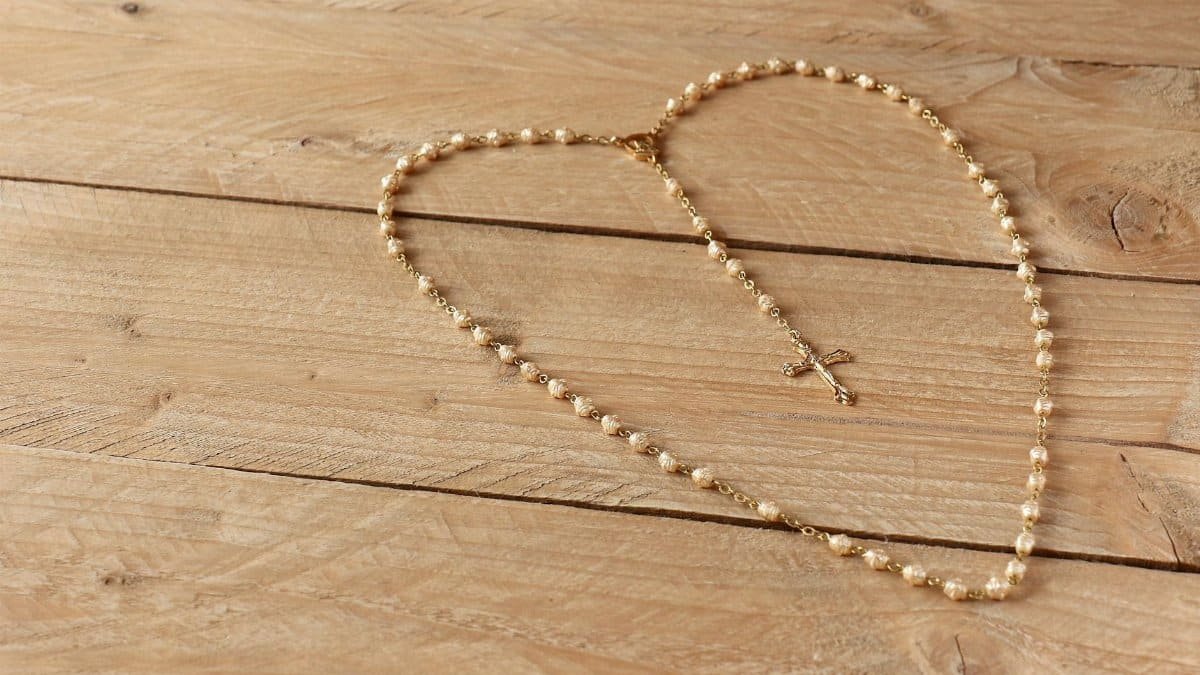 Golden rosary with cross arranged on a natural wooden table, symbolizing faith and spirituality.