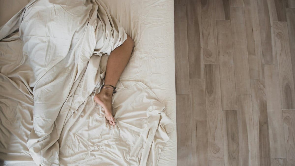 An adult sleeping under soft white sheets in a tranquil bedroom. Top view.