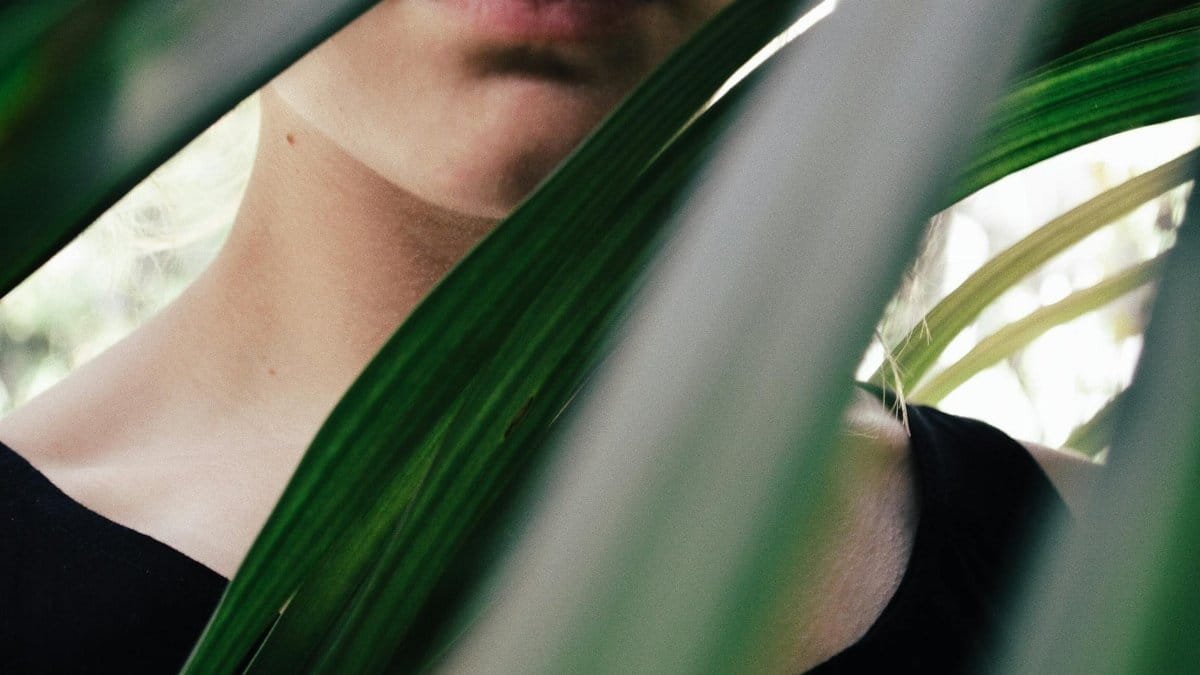 Mysterious portrait of woman partially obscured by lush green leaves.