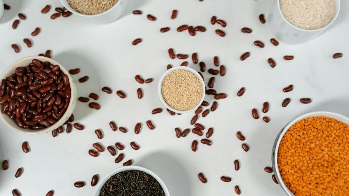 Top view of various grains and pulses in bowls on a white surface.