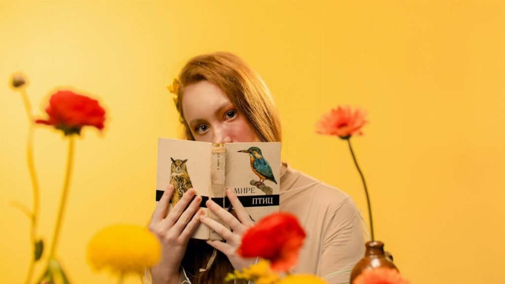 Teen girl with red hair holding a book against a bright yellow floral backdrop.