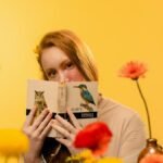 Teen girl with red hair holding a book against a bright yellow floral backdrop.