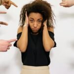 Stressed woman with hands on ears surrounded by pointing fingers, illustrating pressure.