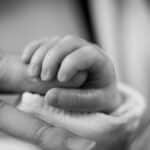 Close-up of a newborn's hand gently holding an adult's finger, symbolizing love and connection.