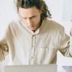 A frustrated man at his desk showing signs of exhaustion and stress in an office setting.