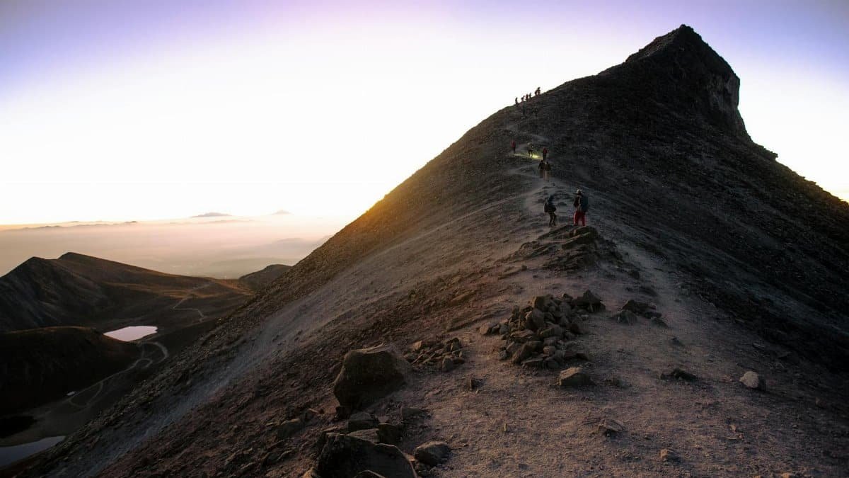 Adventurous hikers ascending a rugged mountain trail at sunrise in Mexico.