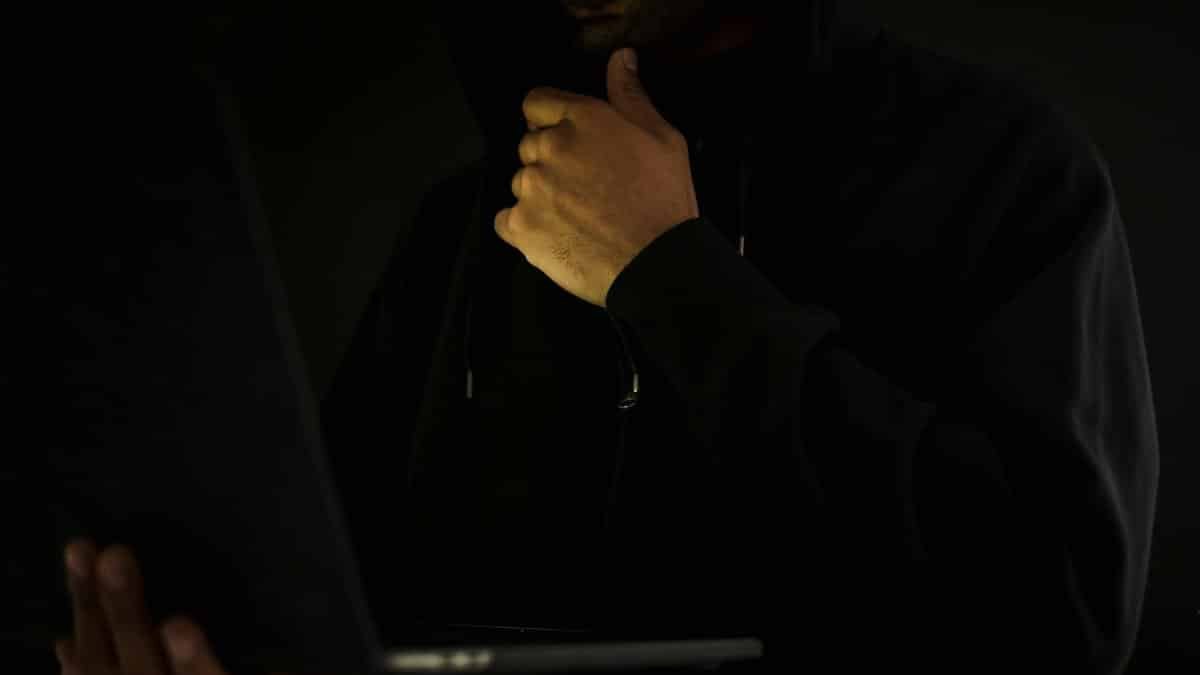 A man in a hoodie uses a laptop in darkness, symbolizing cybercrime and anonymity.