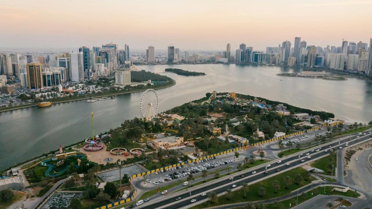 A stunning aerial shot of Sharjah cityscape featuring parks, landmarks, and coastline at sunset.
