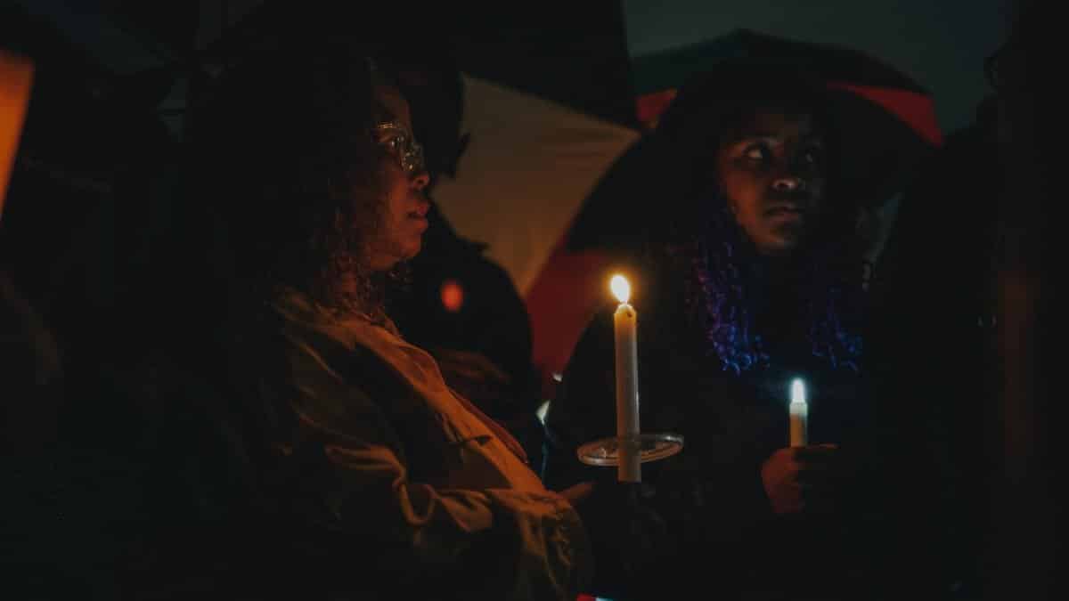 A contemplative candlelight vigil attended by diverse individuals in Tulsa, OK during nighttime.
