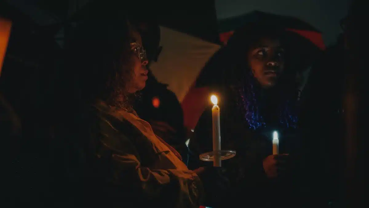 A contemplative candlelight vigil attended by diverse individuals in Tulsa, OK during nighttime.