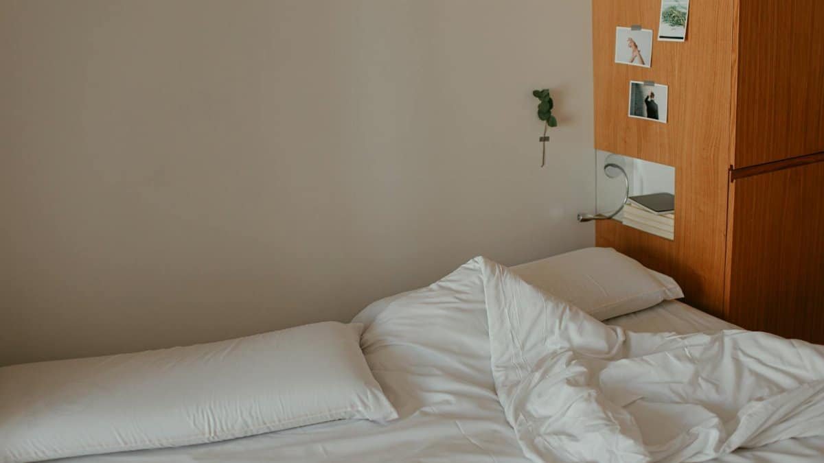 A minimalist bedroom featuring an unmade bed with white sheets and wooden decor.