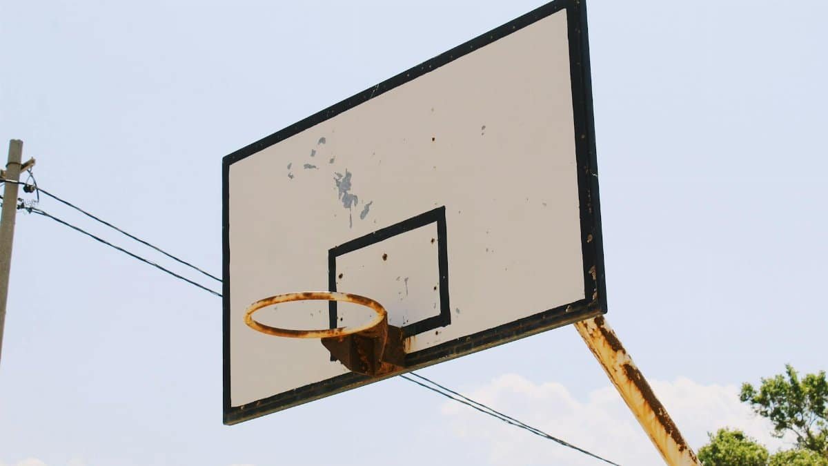 A close-up view of a rusty basketball hoop and backboard against a clear blue sky.