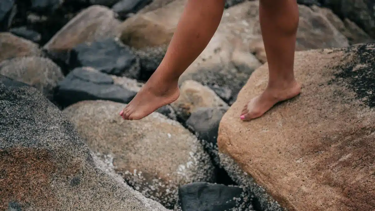 Close-up view of bare feet balancing on rocky terrain outdoors.