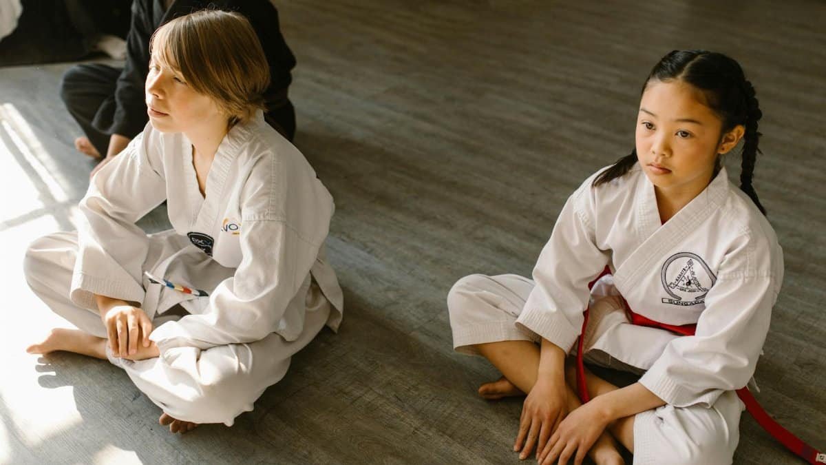 Children sitting on the dojo floor in martial arts uniforms, focused and attentive.