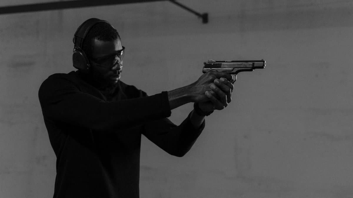 An adult man wearing protective gear practices shooting indoors with a handgun.