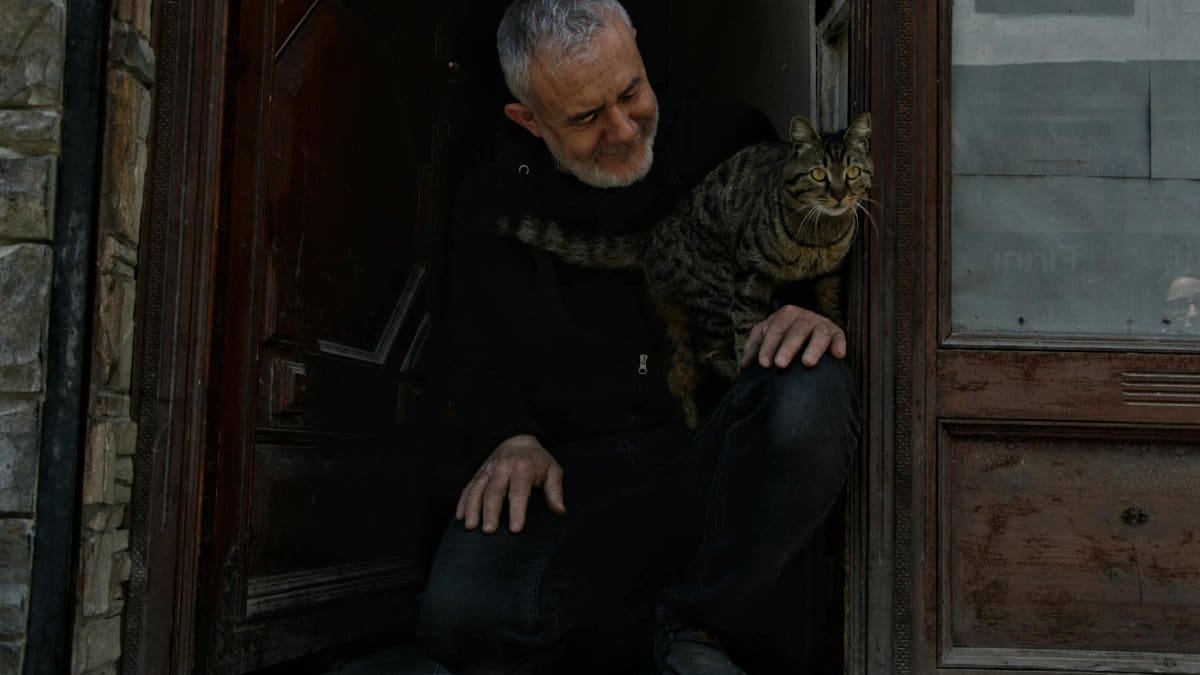 A man and his cat share a quiet moment at a rustic wooden doorway, exuding warmth.