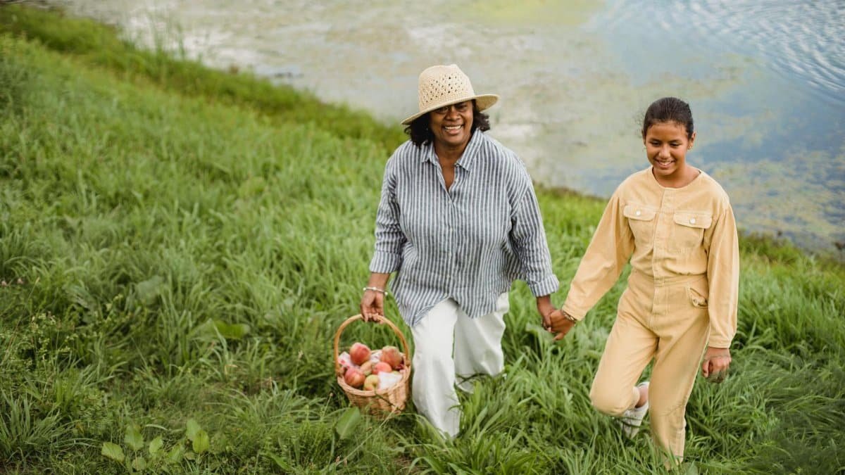 Joyful moment of a mother and daughter walking hand in hand by a riverside, enjoying a summer harvest picnic.