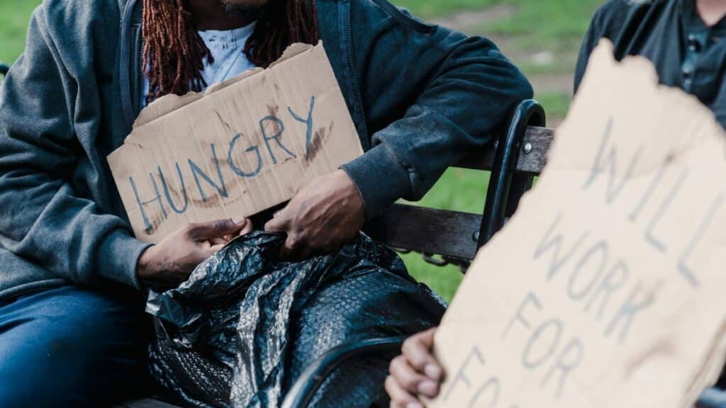 Two individuals holding cardboard signs display the harsh realities of urban poverty.