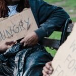 Two individuals holding cardboard signs display the harsh realities of urban poverty.