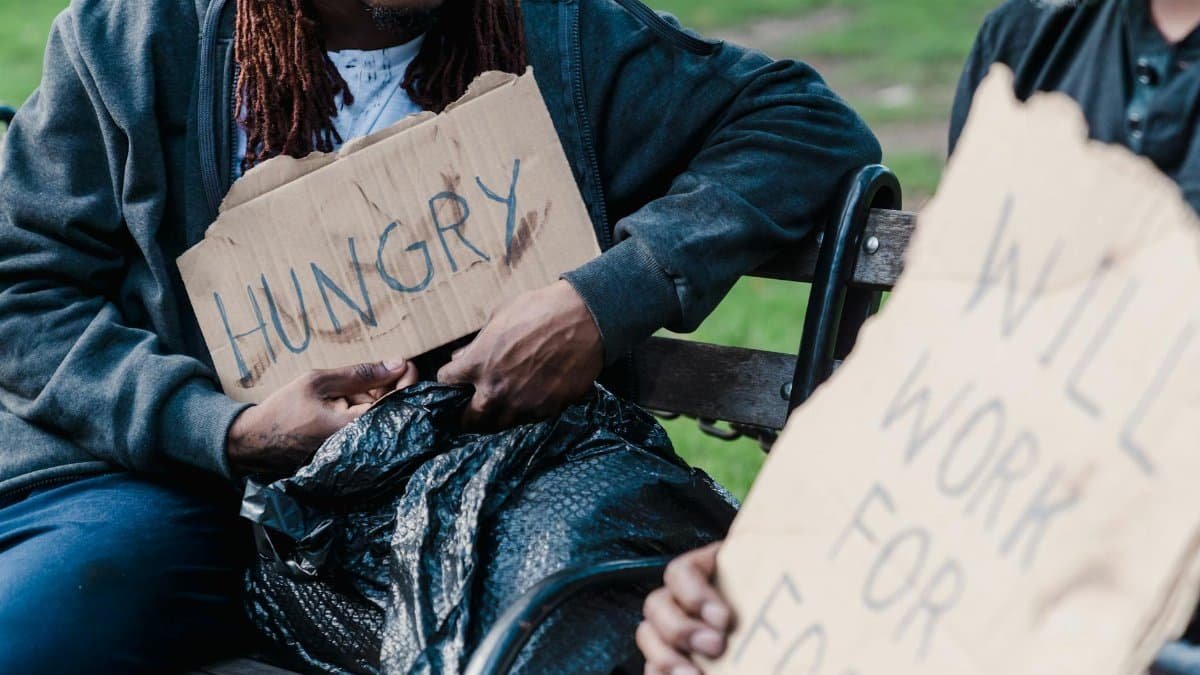 Two individuals holding cardboard signs display the harsh realities of urban poverty.