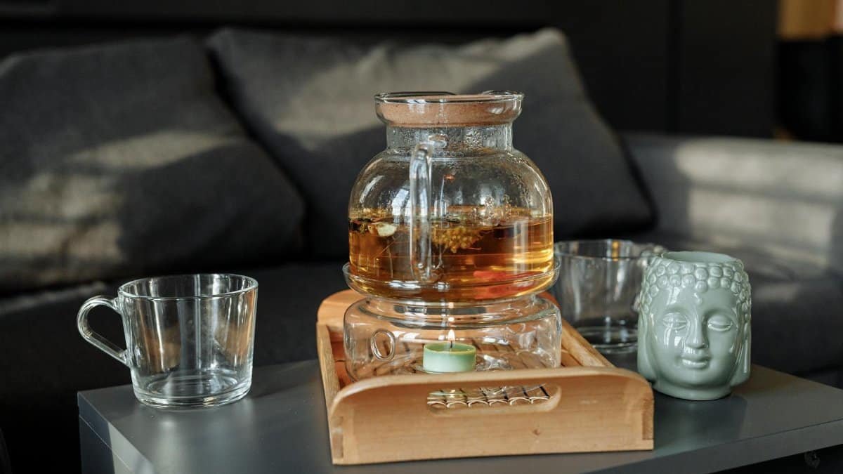 A serene still life of tea in a glass pot with a Buddha mug on a wooden tray.