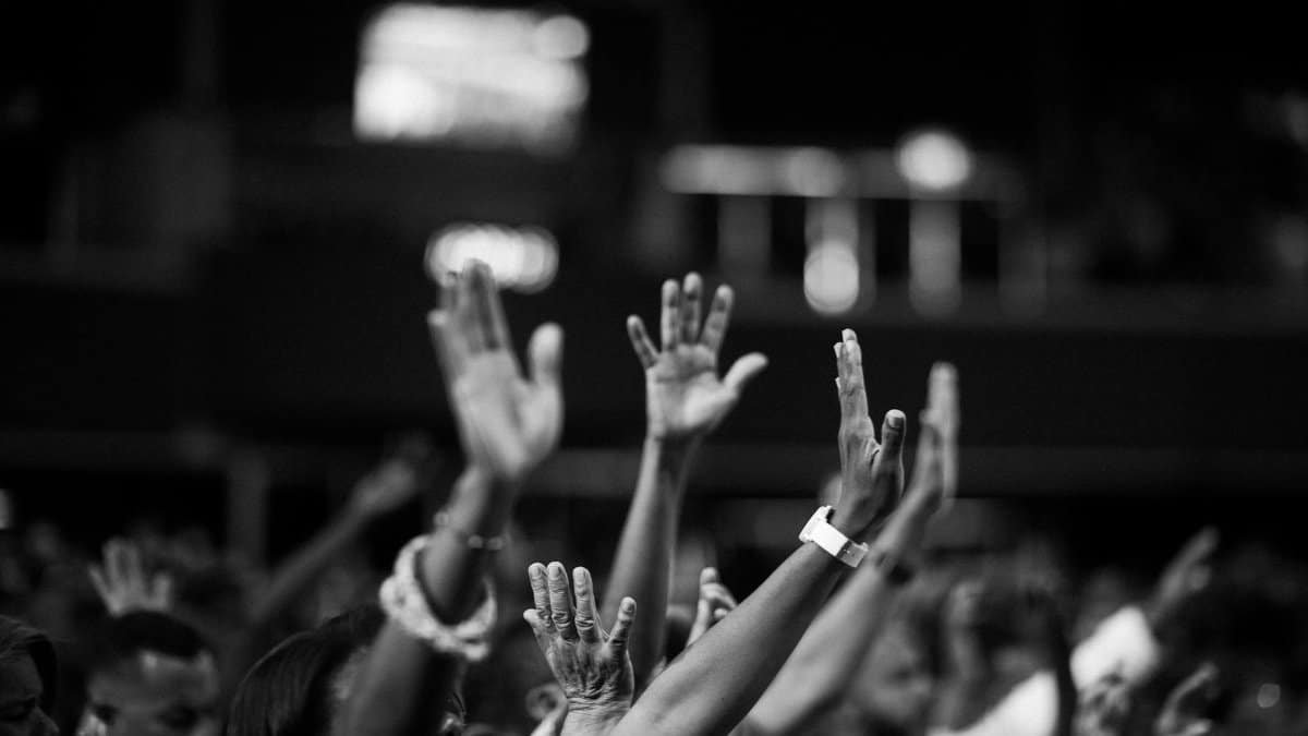 A group of people raising hands in a black and white concert setting, showing unity and celebration.